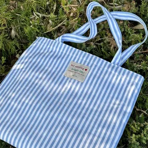 Detailed view of a fresh blue and white striped canvas tote bag resting on green grass