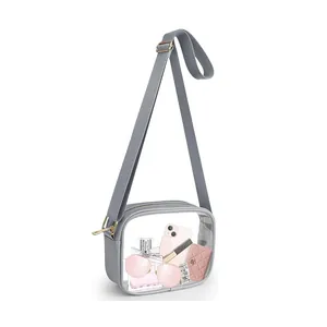 Close-up of clear PVC crossbody bag with adjustable grey strap and pink accessories inside