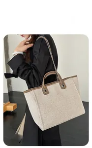 Detail of large canvas tote bag with chain strap carried by model in professional attire.