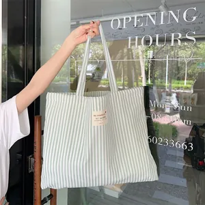 Close-up of a green and white striped canvas tote bag being held in a natural setting.