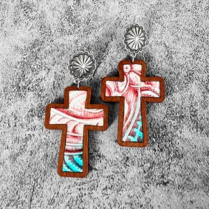 Macro view of western wooden cross earrings with engraved sunflower stud and leather.