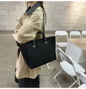 Model carrying a large black canvas tote bag with chain strap in urban setting