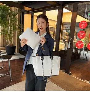Asian model holding a white canvas tote bag with black trim and chain straps outdoors