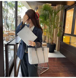 Model carrying a gray canvas chain tote bag and matching clutch in a cafe setting