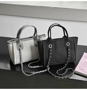 Detailed view of two textured chain tote bags in black and grey, placed on a dark surface