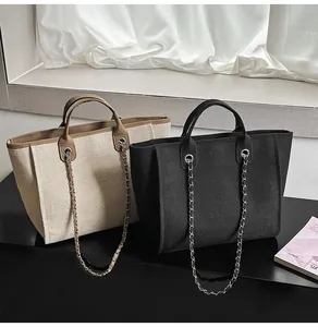 Detail of two large capacity canvas tote bags in beige and black with chain straps