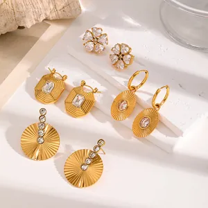 Assorted gold stainless steel earrings with crystals shown on white stone prop.