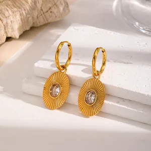 Close-up of elegant gold stainless steel hoop earrings with oval sunburst crystal pendant