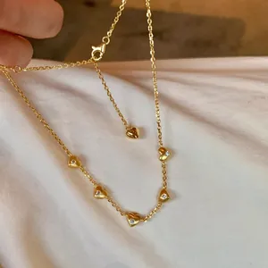 Macro detail of gold clavicle chain necklace featuring five 3D heart-shaped charms set with diamonds