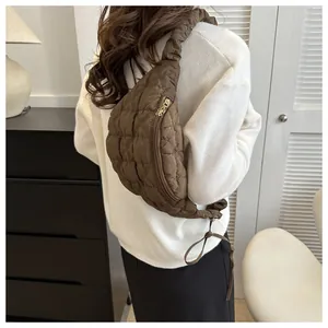 Detailed view of a quilted brown crescent chest bag worn over a white cozy sweater