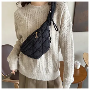 Black quilted crossbody chest bag worn over a beige cable knit sweater for fashion.