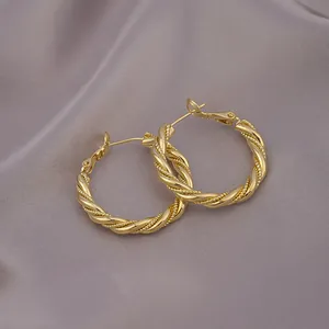 Nahaufnahme der goldenen gedrehten Mobius-Creolen auf elegantem grauem Satinstoff