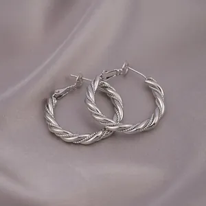 Exquisite Nahaufnahme von silbernen gedrehten Möbius-Creolen auf grauem Seidenstoff