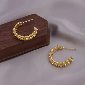 Detailansicht goldener gedrehter Creolen mit filigranem Design auf seidigem Hintergrund.