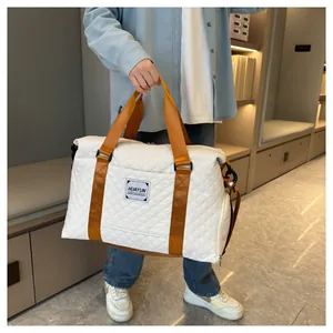 Grand sac de voyage matelassé blanc avec anses marron tenu par une personne stylée.