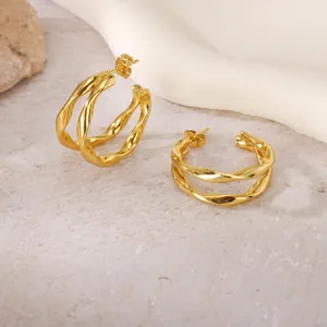 Détail rapproché de boucles d'oreilles créoles torsadées dorées en acier au titane.