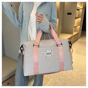Détail d'un sac de voyage gris matelassé avec des sangles roses tenu par une personne