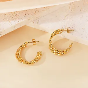 Détail d'élégantes boucles d'oreilles créoles torsadées en acier inoxydable doré.