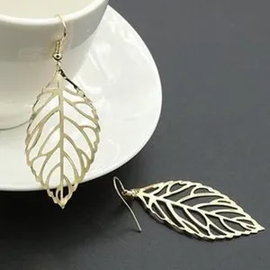 Detailed view of elegant gold-toned leaf hollow-out drop earrings hanging on a white cup rim.