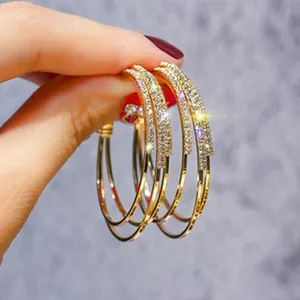 Close-up detail of elegant gold triple hoop earrings encrusted with sparkling crystals.