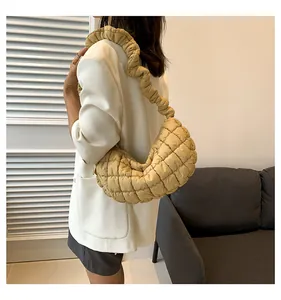 Detail view of a beige quilted puffer dumpling bag with a unique ruffled shoulder strap.