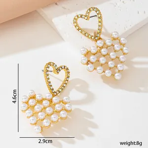 Detail view of gold heart-shaped earrings decorated with white pearls and rhinestones