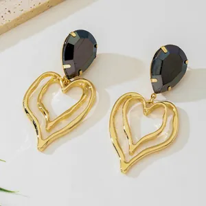 Close-up of gold heart earrings with dark pear-shaped crystals and layered design.