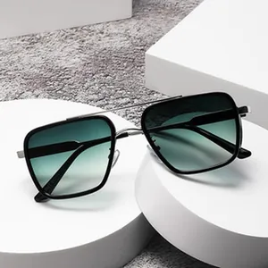 Close-up of square metal sunglasses with green gradient lenses on white display stands.