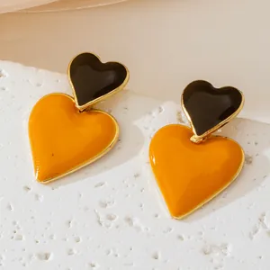 Macro detail view of elegant heart-shaped drop earrings with black and orange enamel