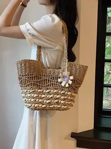 Große Strandtasche aus Strohgeflecht mit Blumenanhänger, getragen von einem Model.