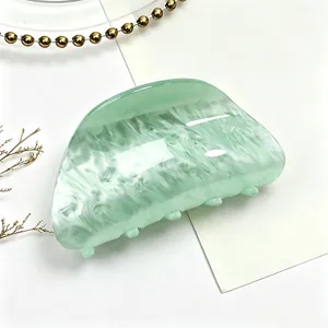 Detail of a green acrylic hair claw clip with a white water ripple marble pattern.