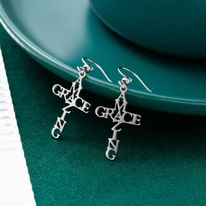 Close-up of silver titanium steel cross earrings with Amazing Grace cutout detail.