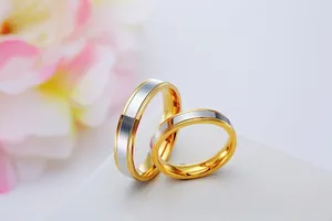 Two-tone gold and silver stainless steel couple rings set on white surface