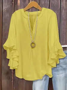 Macro view of yellow V-neck blouse featuring tiered ruffle sleeves and necklace accessory