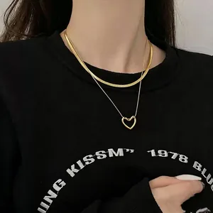 Primo piano di elegante collana a doppio strato in oro con ciondolo a cuore e catena snake.