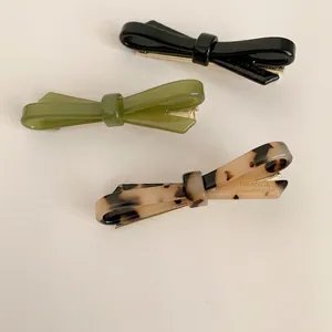 Macro view of high-end acetate bow hair clips in black, olive green and tortoise shell.