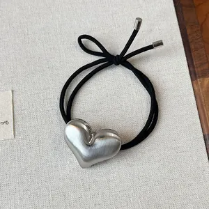 Close-up detail of minimalist metallic heart hair tie with a brushed silver finish