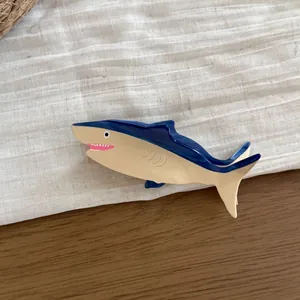 Close-up detail of a large shark-shaped acetate hair claw clip on a textured white fabric.
