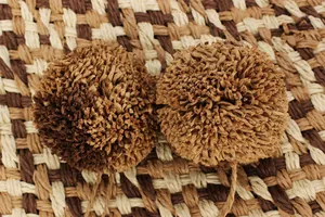 Macro detail of decorative paper string pom-poms on a woven summer straw handbag.