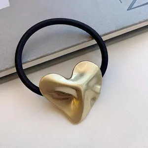 Macro view of a gold minimalist heart-shaped metal ornament on a black hair tie.