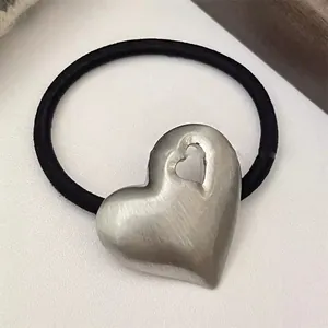 Close-up detail view of a minimalist metal heart charm on a black elastic hair tie