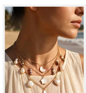 Detail view of a layered gold necklace featuring heart moon and flower pearl pendants on model