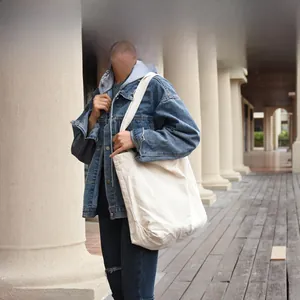 Detailed view of a minimalist white canvas tote bag worn by a model in an outdoor setting
