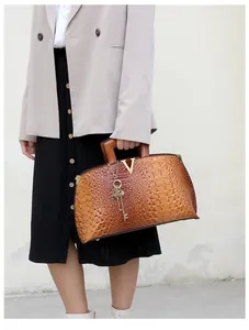Woman in beige blazer holding brown crocodile embossed handbag with gold V logo