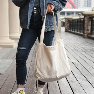Close-up of a person carrying a large beige canvas tote bag in a casual outdoor setting