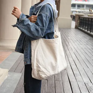 Detailed side view of a minimalist cream canvas tote bag on a model