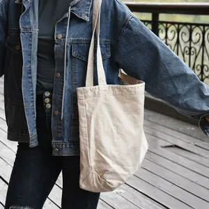 Close-up detail of a minimalist white canvas tote bag worn over the shoulder in a street setting