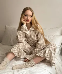 Fashion model wearing a brown gingham pajama set with ruffle hems on soft white bedding