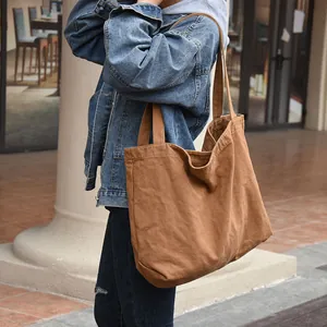 Detail view of a large brown canvas tote bag carried by a model in a casual street setting.