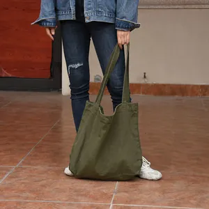 An olive green canvas tote shoulder bag held by a model in a casual street setting.